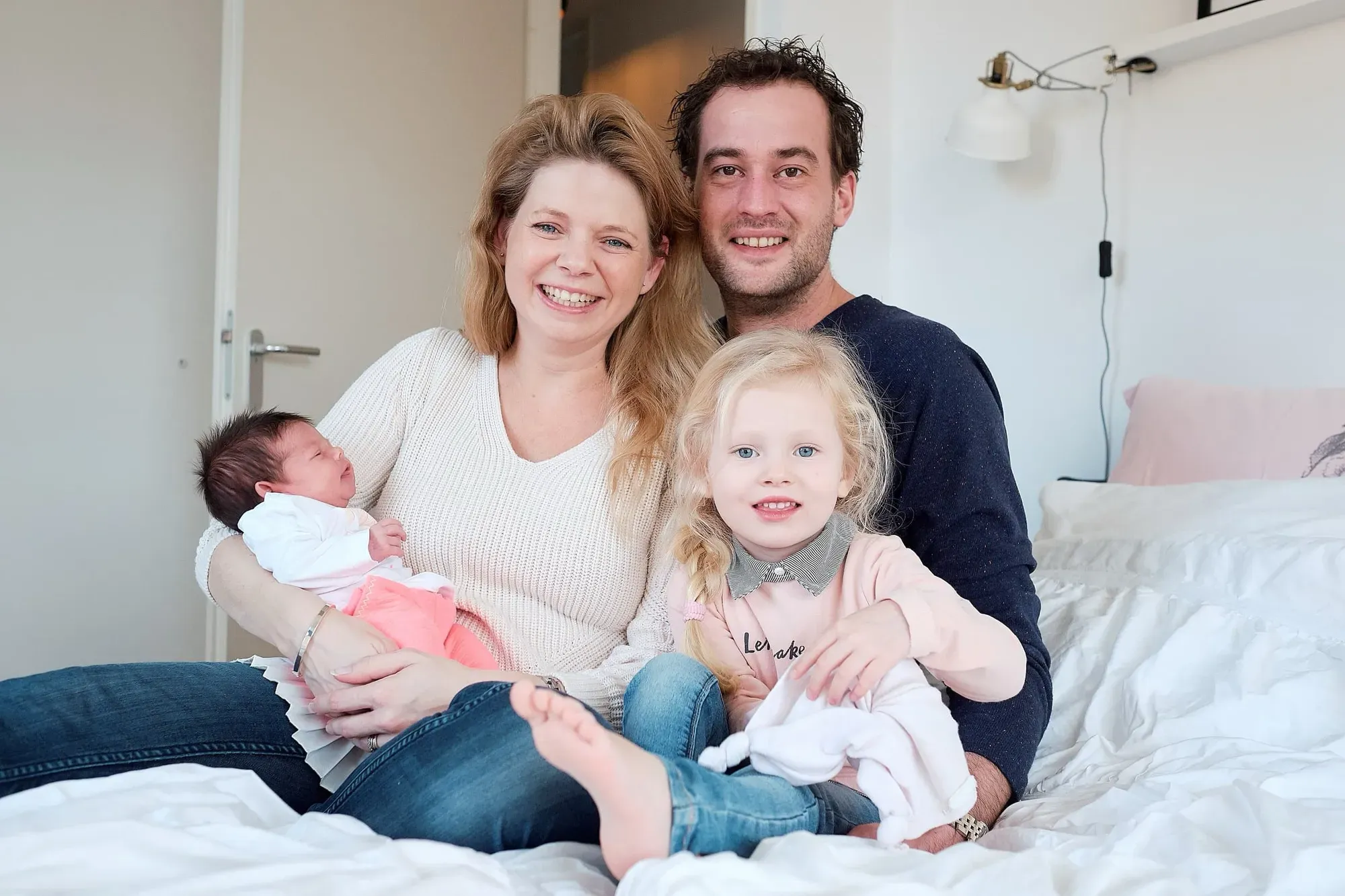 Ouders zitten met de baby en hun peuter op bed