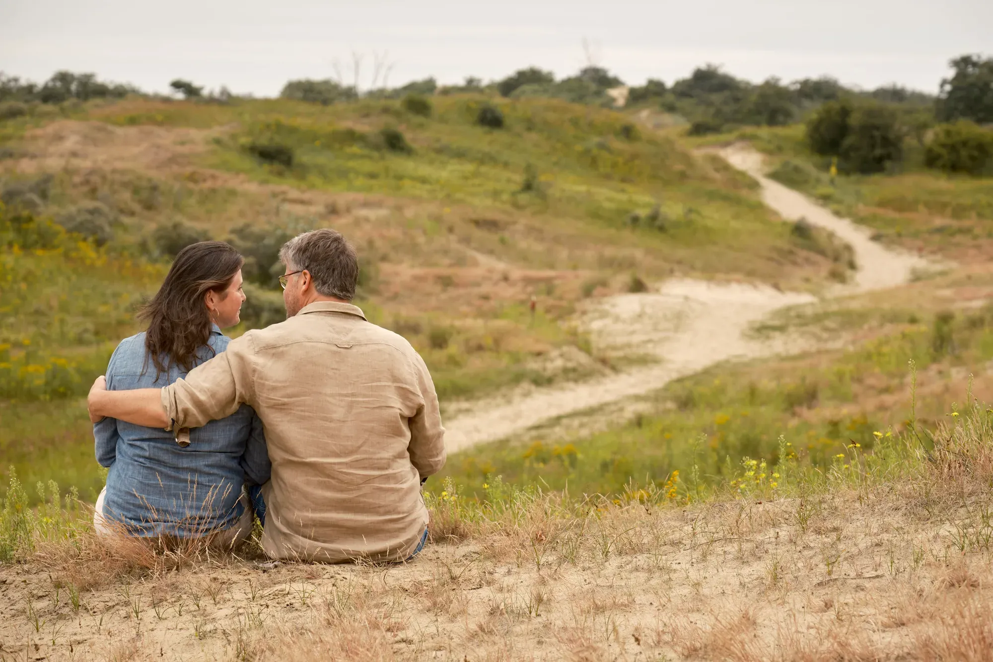 Stel zit in het gras naast een slingerend zandpad aan het eind van de middag