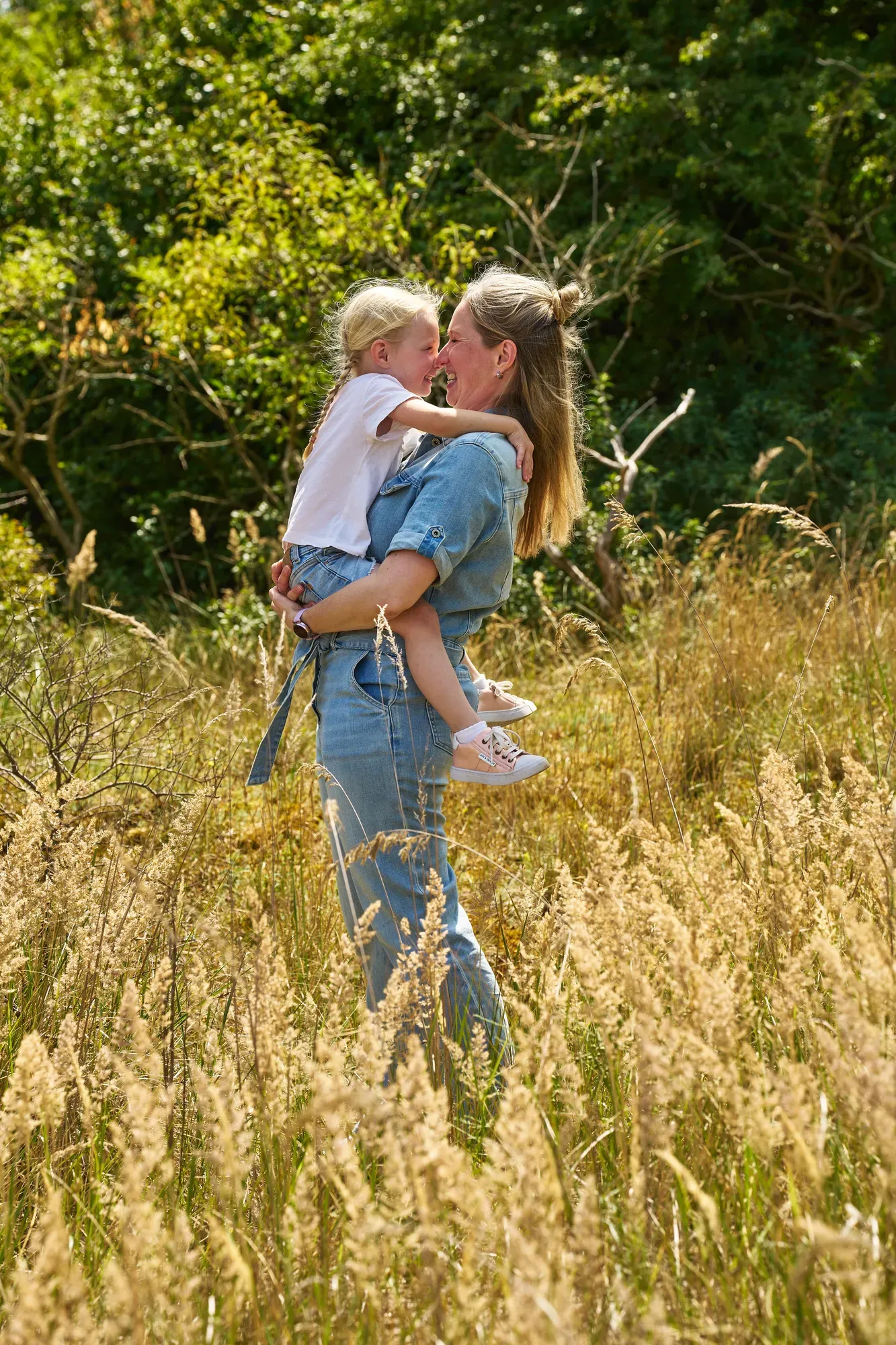 Moeder knuffelt haar kind in het hoge gras in de duinen