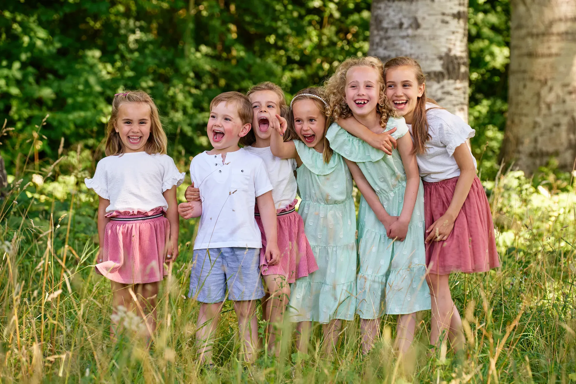 Zes kinderen lachen samen in het hoge gras bij een boom in het Westerpark