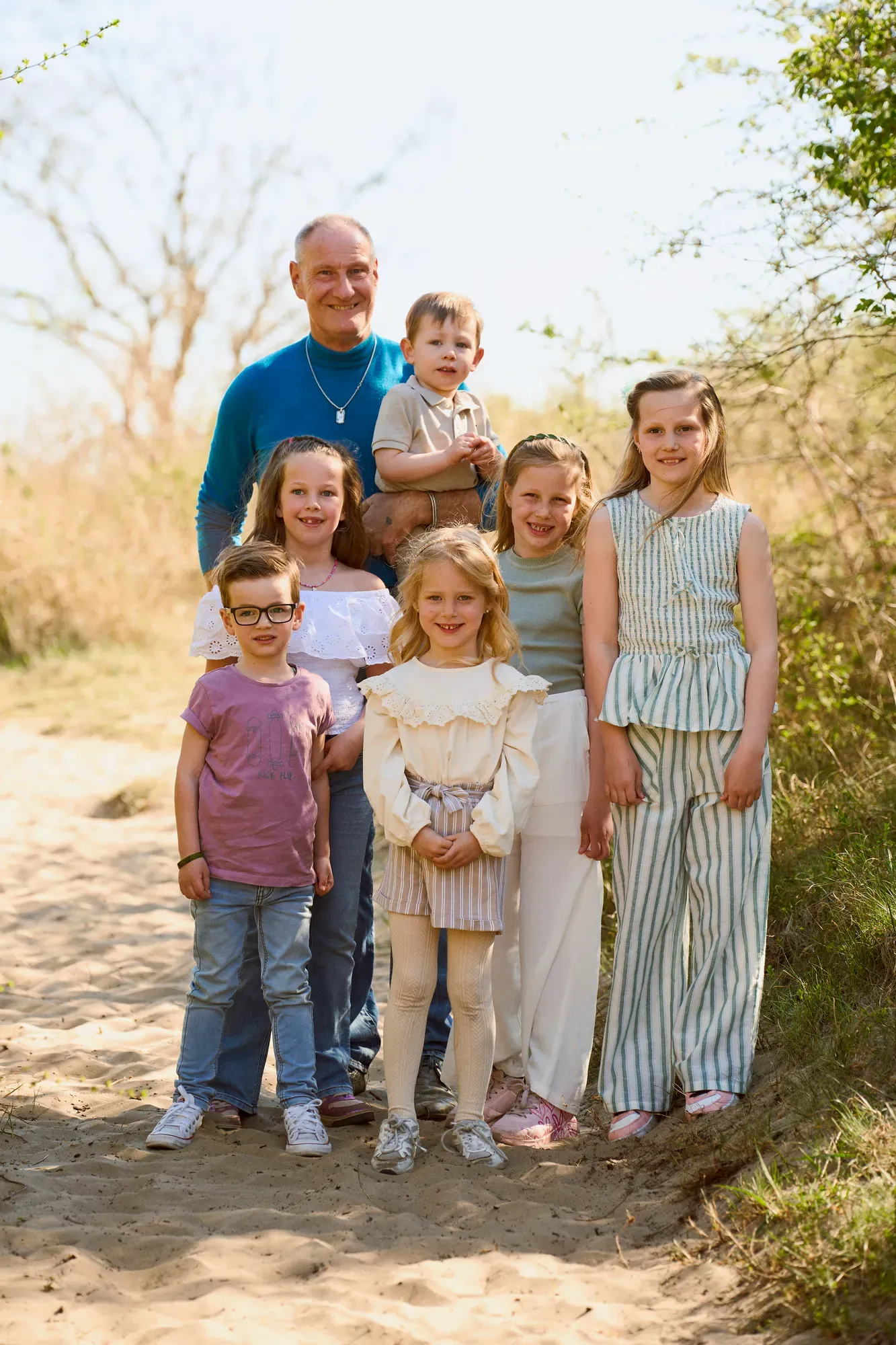 Opa staat met vier kleinkinderen op een zandpad in de duinen in april