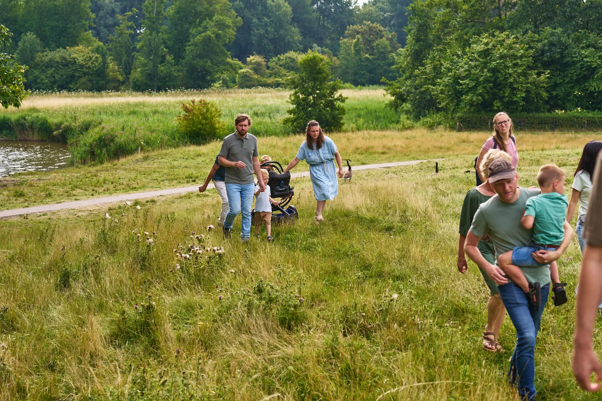 Familie loopt met kinderen en een kinderwagen over het gras langs het water in het Westerpark