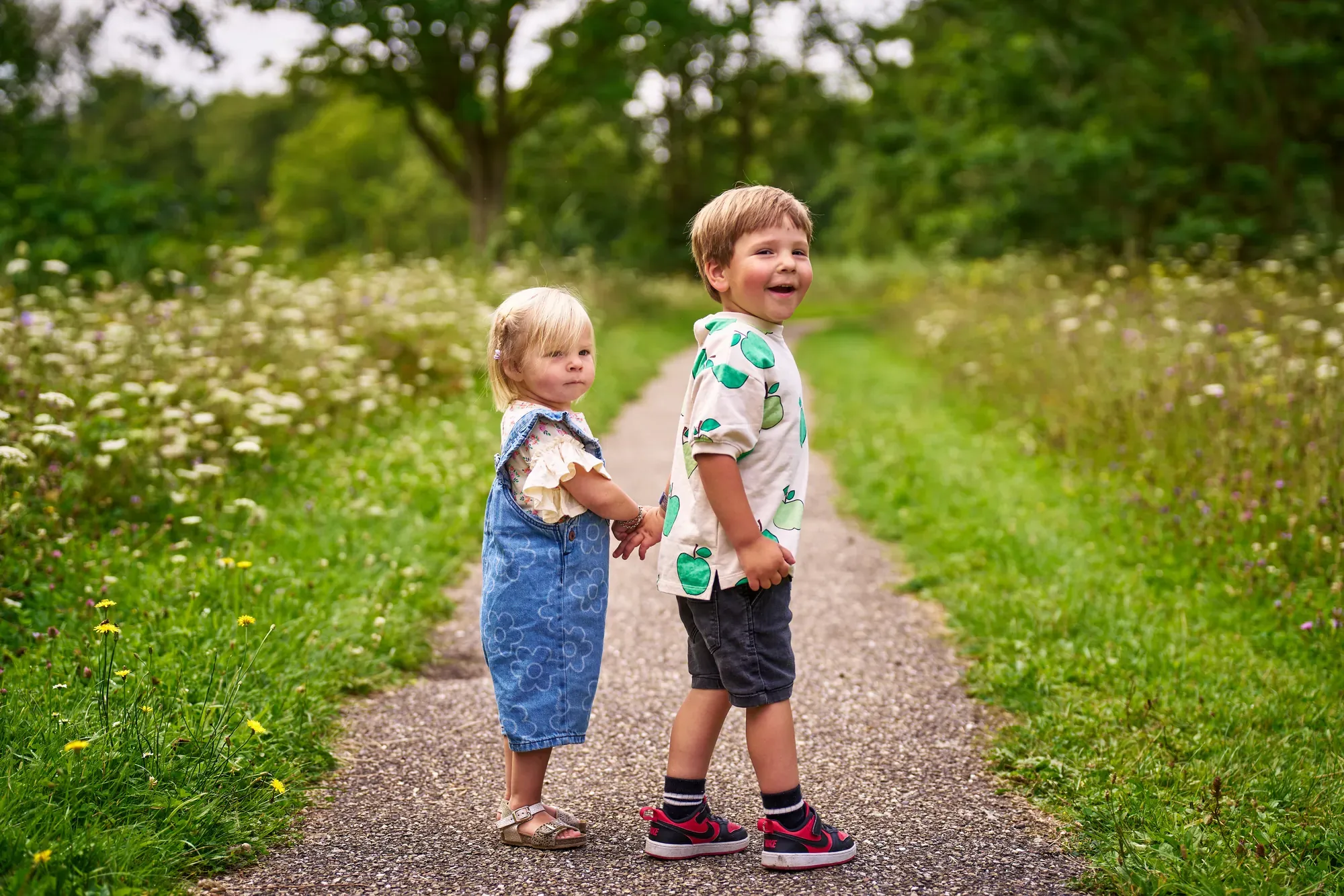 Broer en zus staan lachend op een wandelpad tussen het groen in het Westerpark