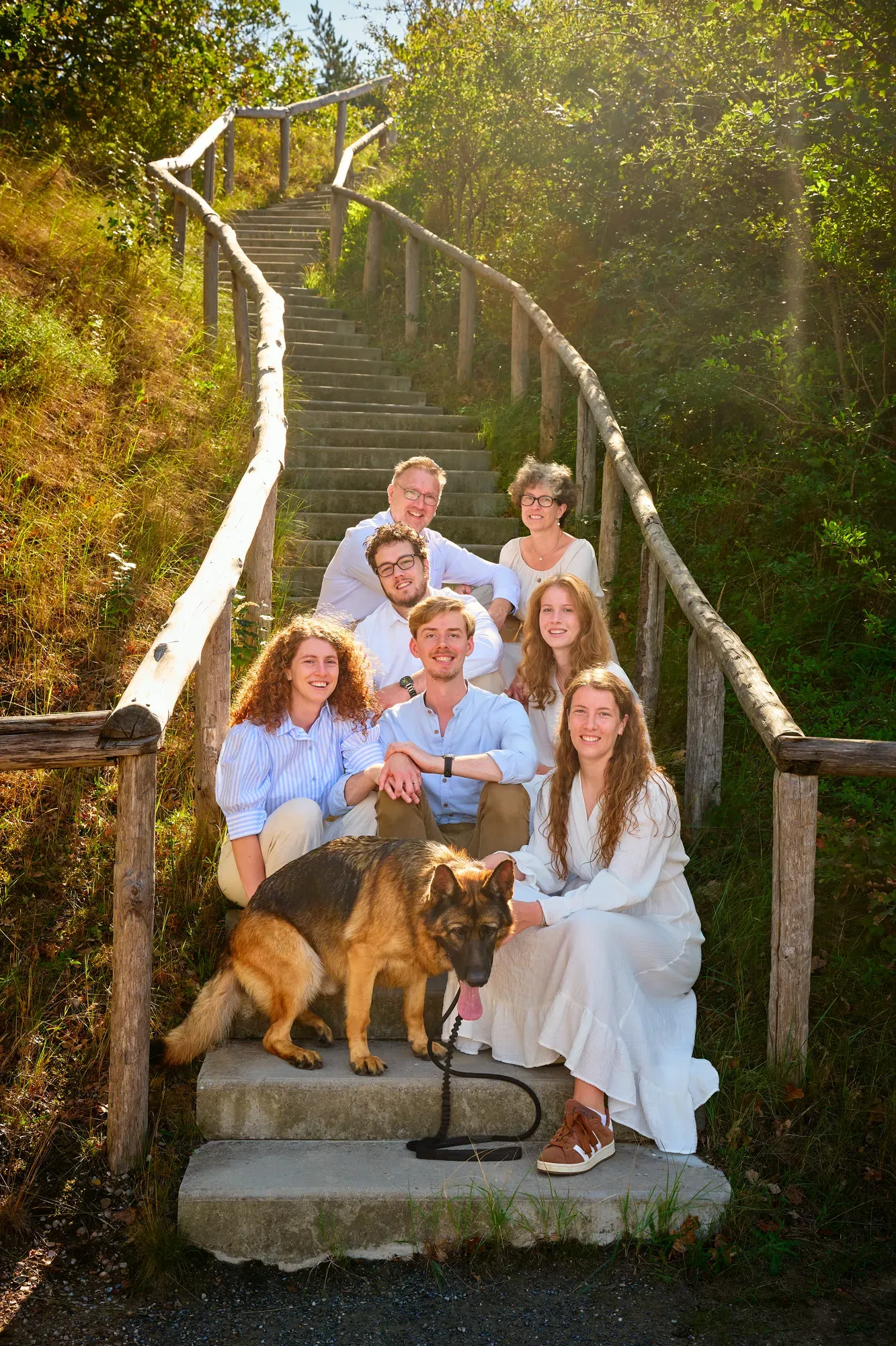Familie met hond zit samen op een trap met houten leuning in de duinen