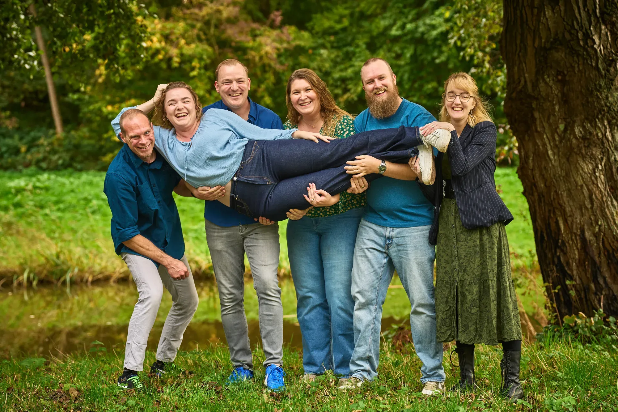 Familie tilt lachend een familielid op onder de bomen in het Westerpark op een bewolkte herfstdag