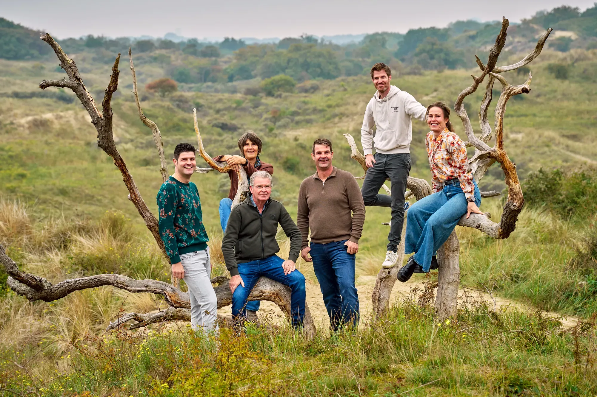 Familie poseert rond de kale takken van een dode boom in de duinen
