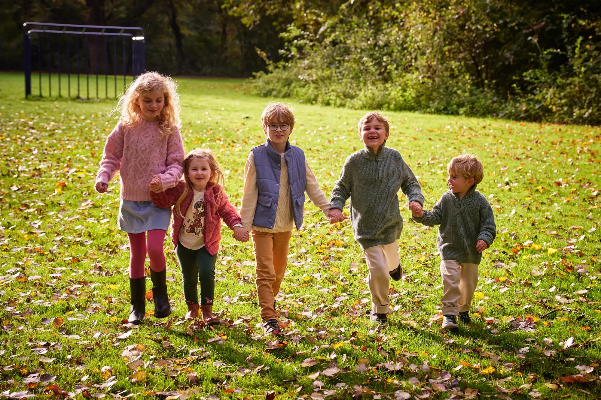 Vijf kinderen lopen hand in hand over het gras met herfstbladeren in het Westerpark