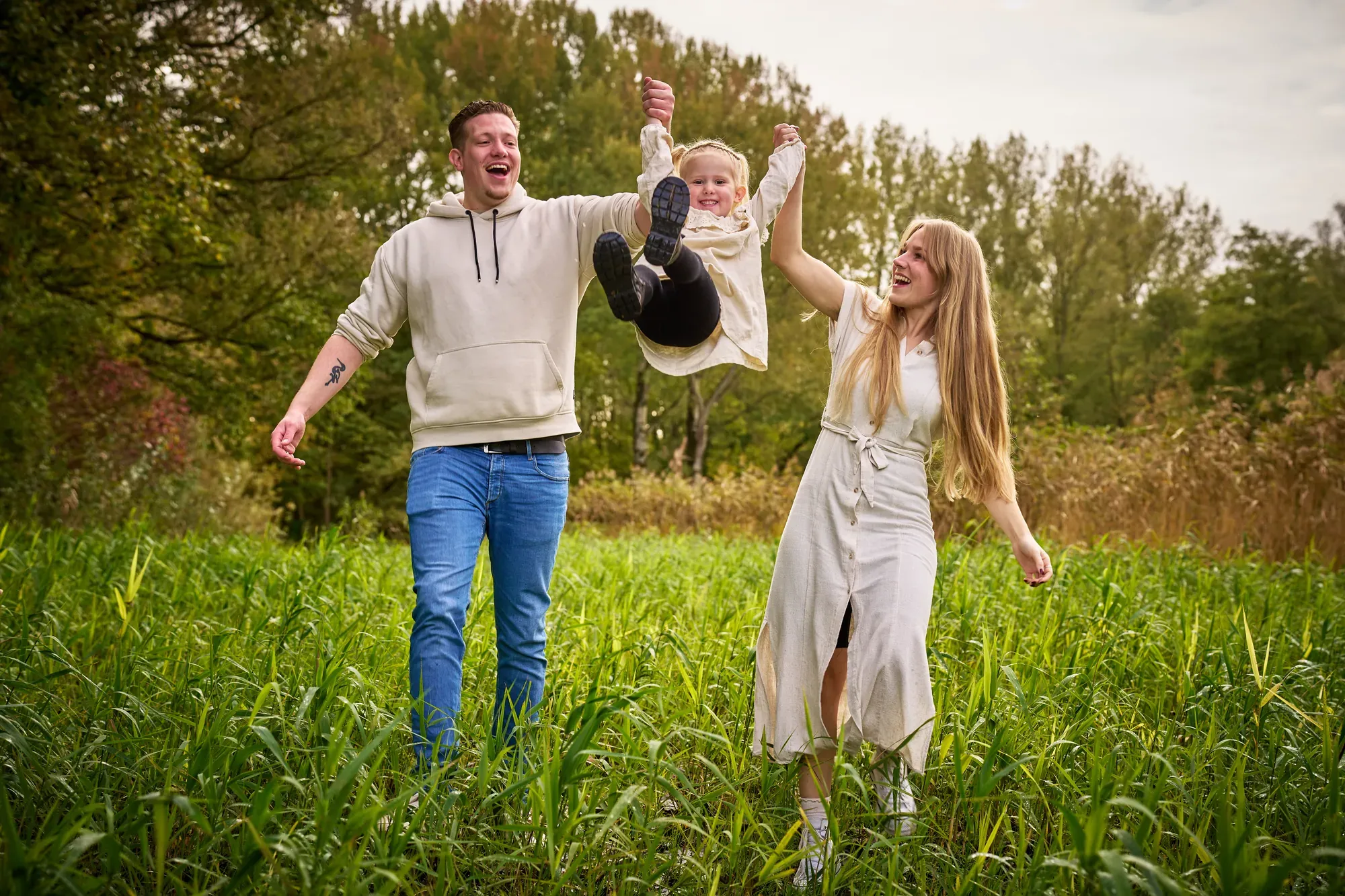Ouders zwaaien hun dochtertje tussen zich in door de lucht in het Westerpark