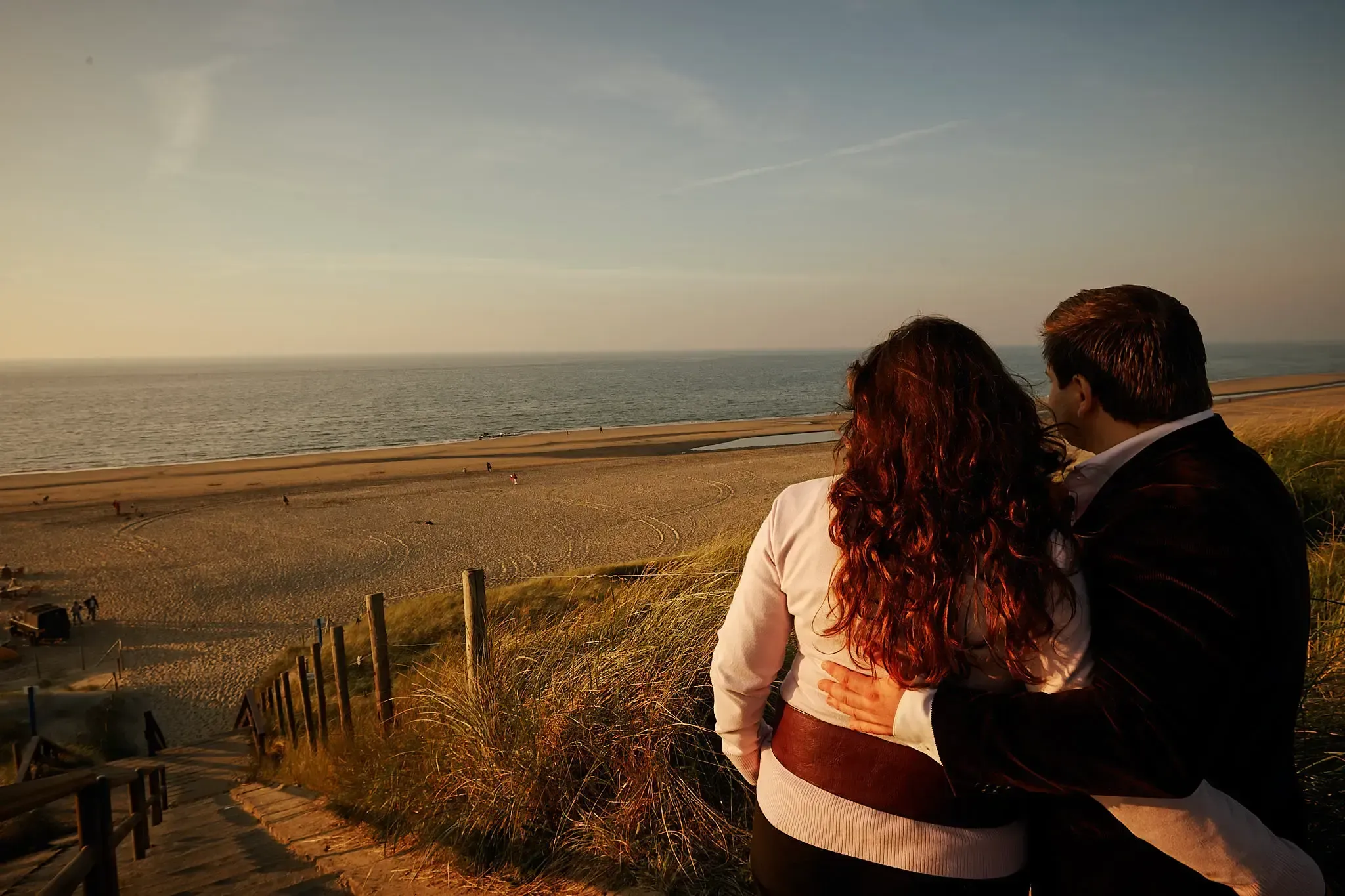 Uitkijkend over het strand vanaf de duinen, met de zee al in avondlicht.