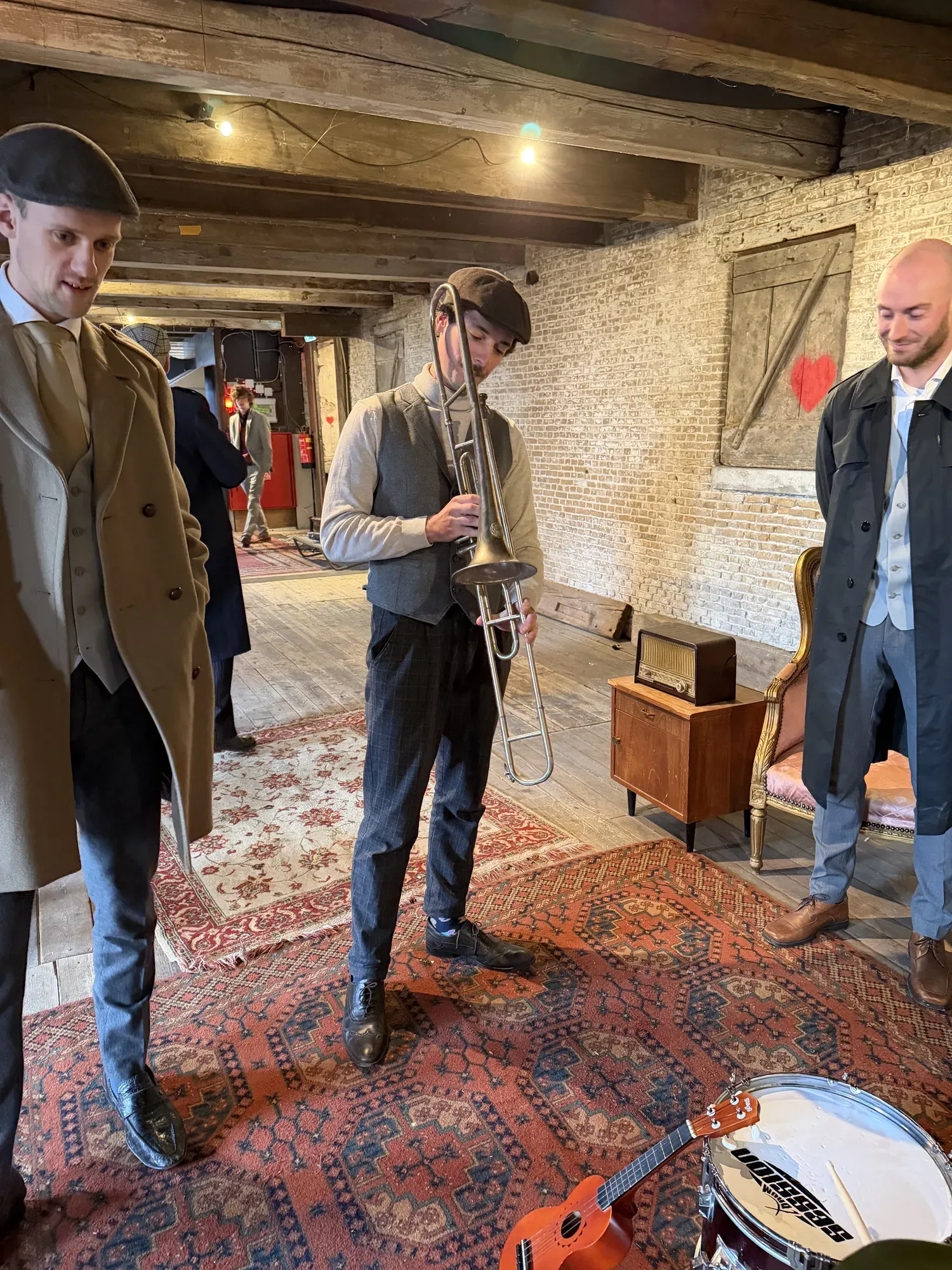 Drie mannen in kostuum, één speelt trompet, tussen de opnames door